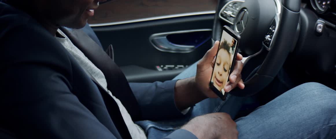 A man sits in the drivers seat of a vehicle video chatting with a small child on his cell phone