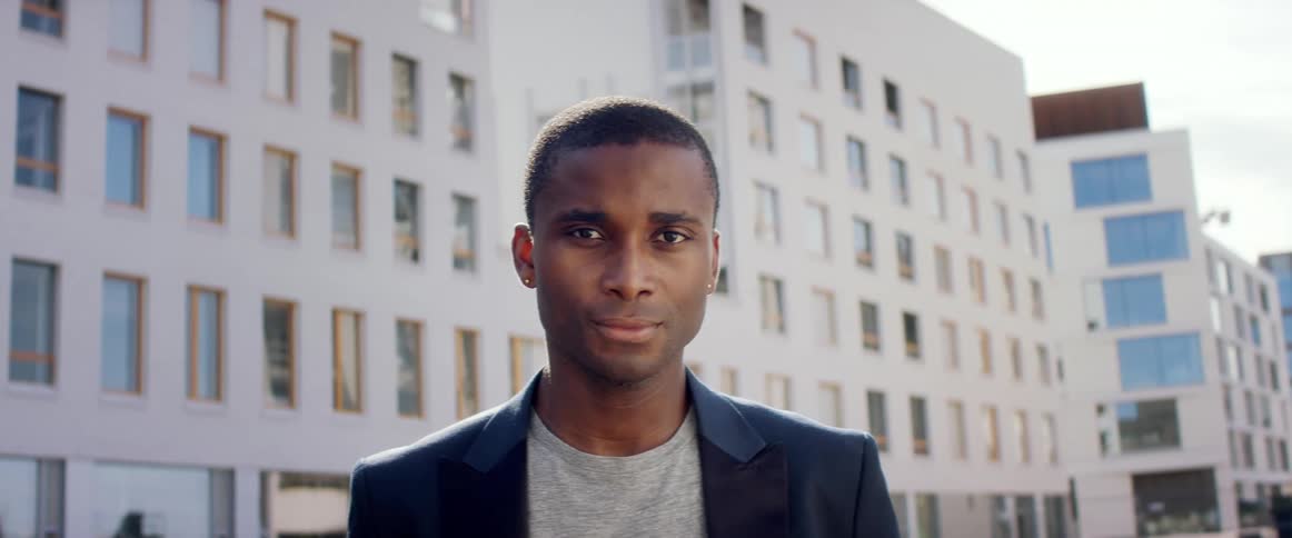 Young man wearing a blazer standing in front of a building looks at the camera