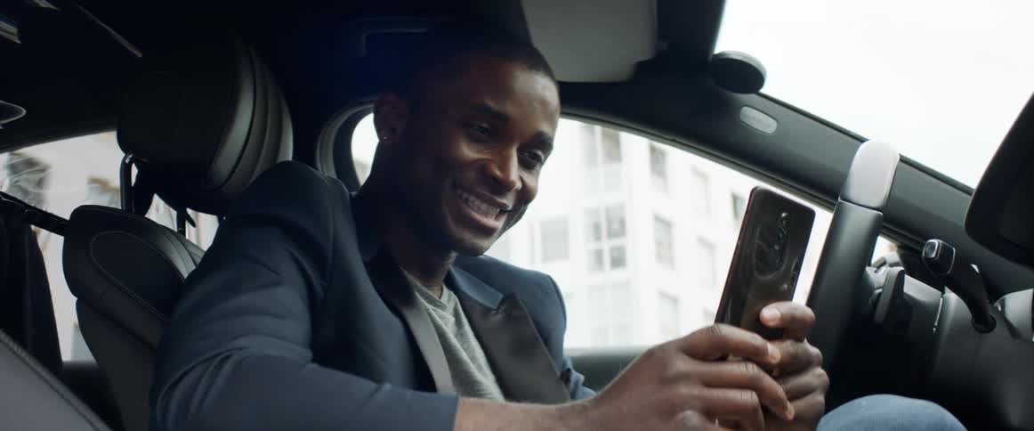 A man sitting in his car laughs while video chatting on a his smartphone