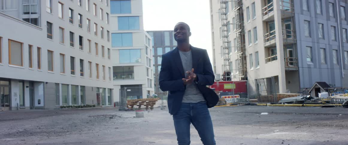 A man rubs his hands together while walking around a construction site in a metropolis on a sunny day