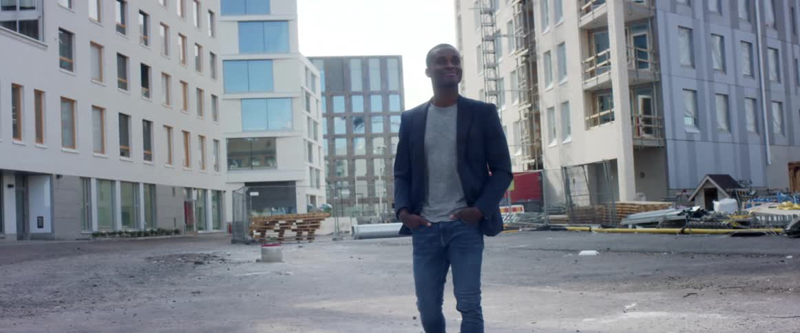 Man in blazer and jeans walks across parking lot near building under construction and stacked materials