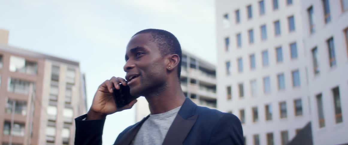A man is standing in a downtown city and talking on a cellphone