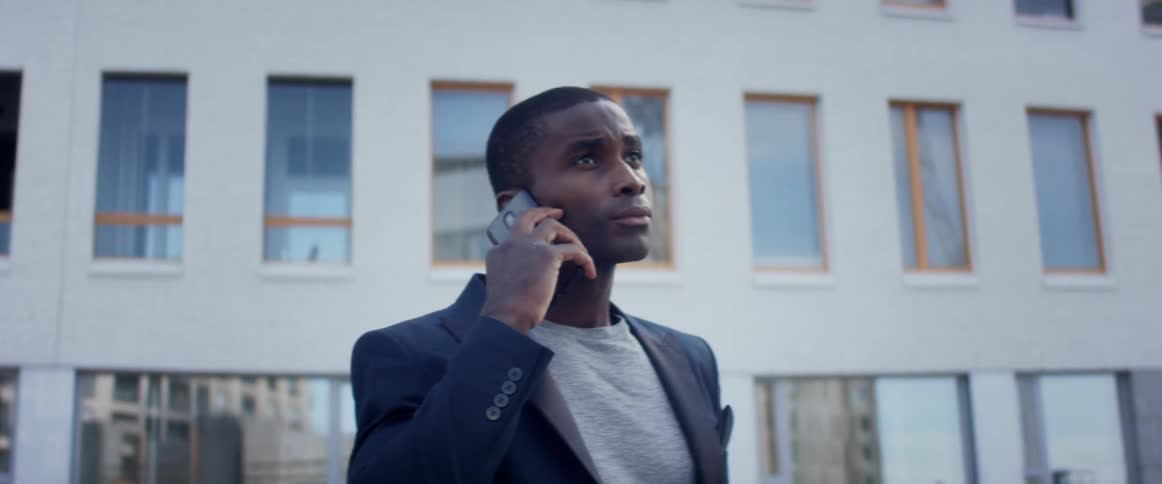 A man standing in front of an apartment building makes a phone call on his cell phone