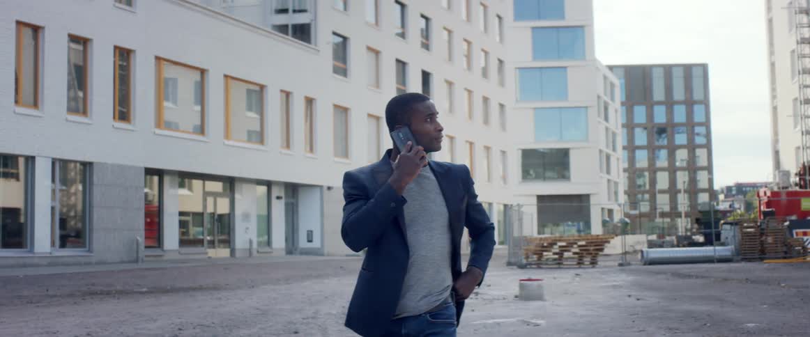 A man is walking in a city and talking onhis cell phone