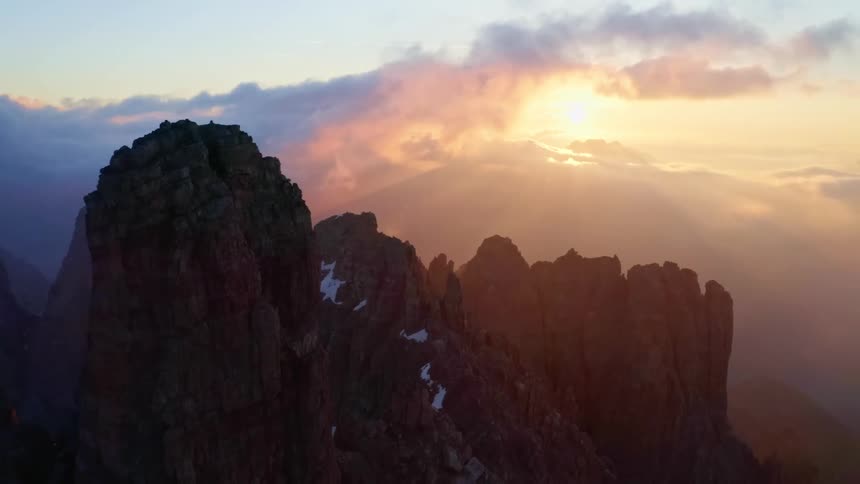 The sun peeks through dense clouds and a light haze over a mountain range