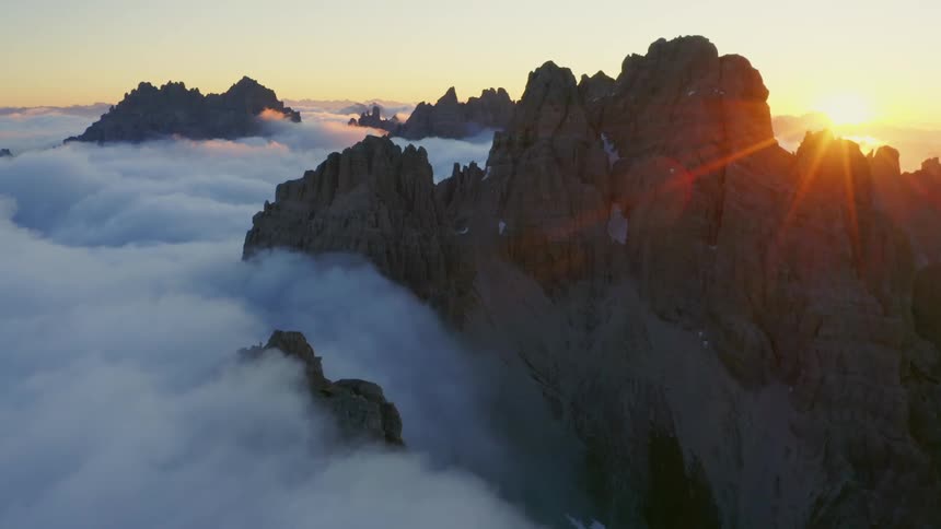 The low sun shines on the peak of a mountain looming over a sea of dense fog