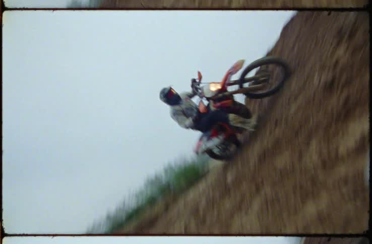 Motorcyclist rides motorcycle up steep dirt slope as fog covers trees on horizon