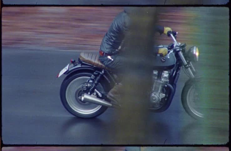 Male motorcyclist with a helmet a black leather jacket and jeans rides a motorcycle on a road through a forest