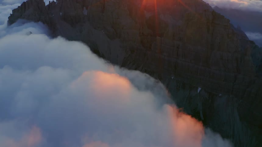 A cliff with a mountain range the sunset sky and clouds in the background