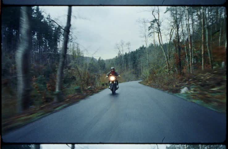 Man with a helmet and a leather jacket rides a motorcycle on a road through a forest
