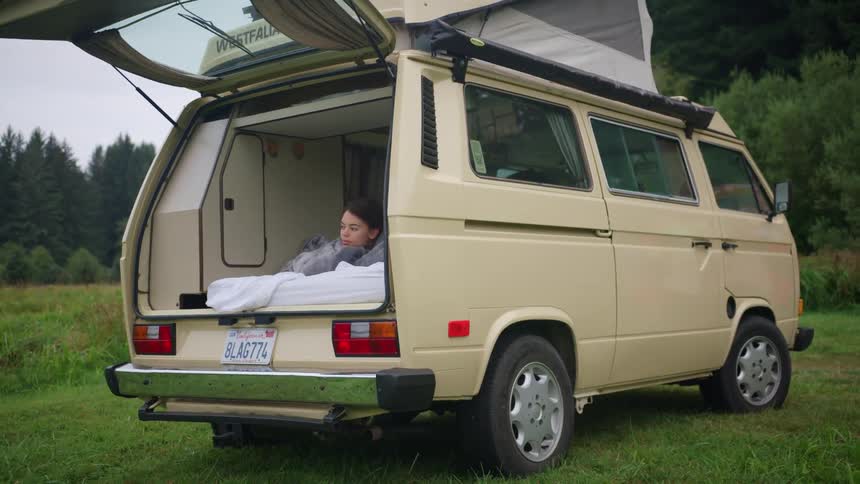 A teenage girl lies in the back of her van parked in a grassland
