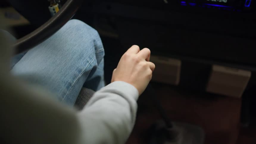 Woman uses gear shifter to switch gears while sitting in a car with the radio on