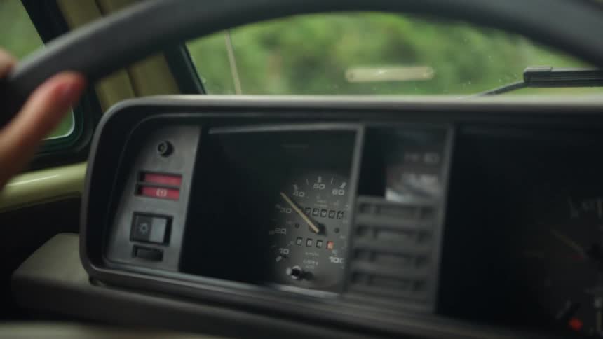 An older vehicle drives past tree lined roads in the countryside