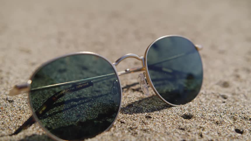 A pair of sunglasses lying on sandy ground on a sunny day