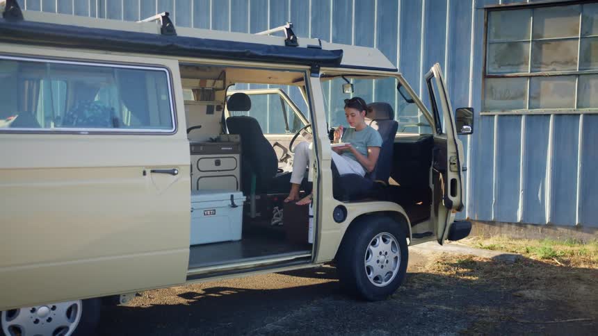 A young woman sits in a van and eats