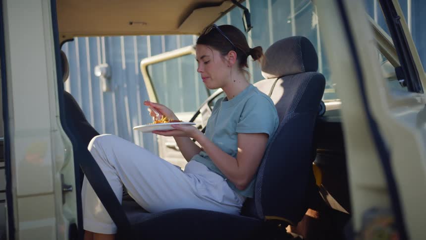 A woman sits backwards in a vehicle eating from a plate of food