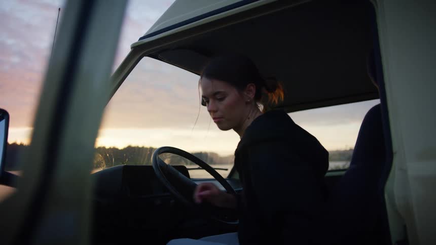 A teenage girl gets out of her van that is stopped on the shore