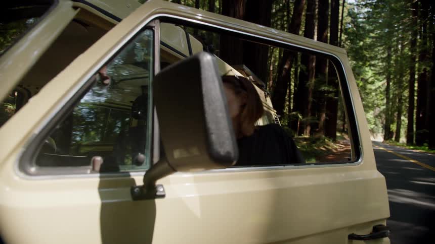 Woman with shorts a black t shirt and brown hair opens the door and gets in the van on the forest road
