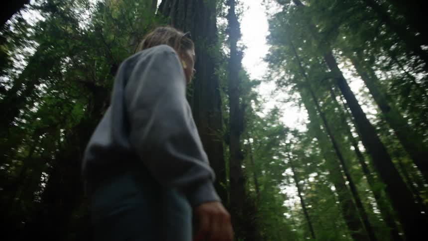 Woman walks through conifer forest looking around