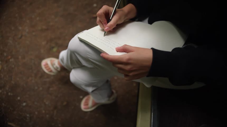 A woman is sitting outdoors and writing in a journal