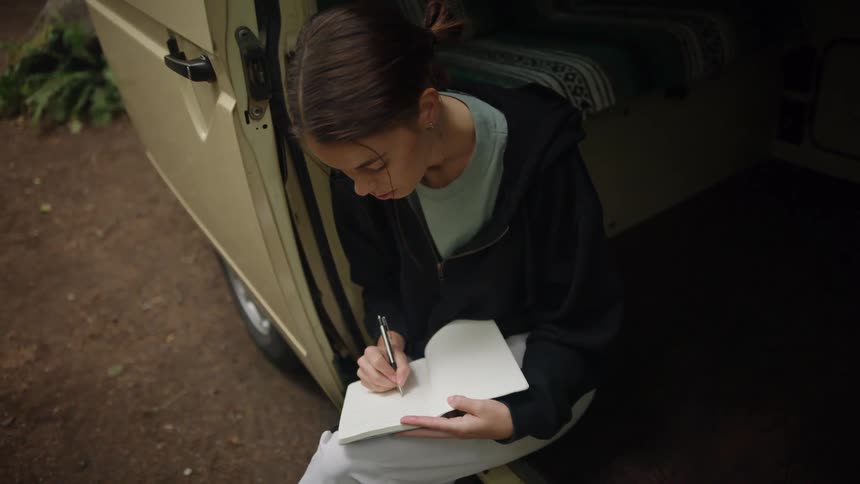 A woman sits in an open van writing in a notebook