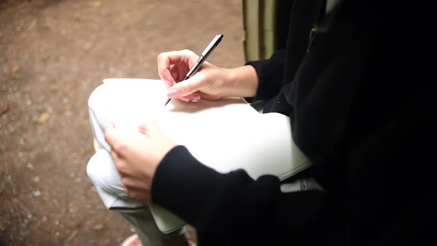 A teenage girl sitting outside writing in a notebook