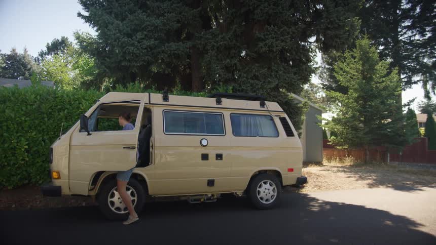 Woman gets into drivers seat of van parked on street near hedge