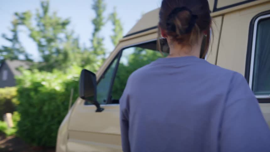 Woman adds bag to items in back of vehicle parked near house before getting into vehicle to start it