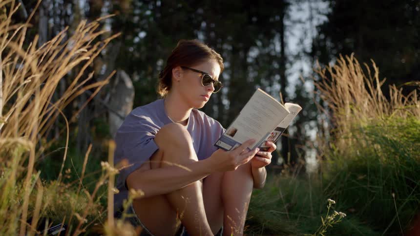 A young girl sitting outside reading a book