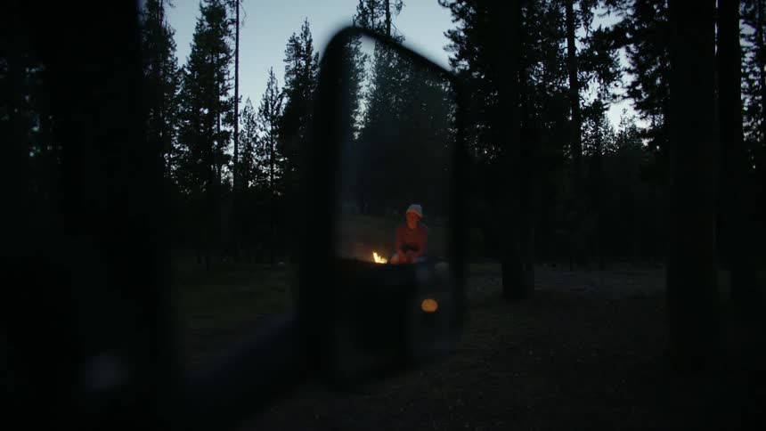 A person is sitting in the woods by a bonfire
