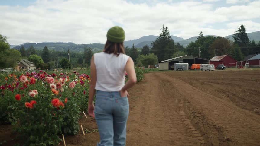 A woman walks in a farm field beside a row of flowers