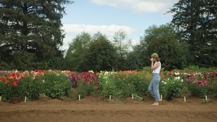 A woman walks past a garden filled with flowers