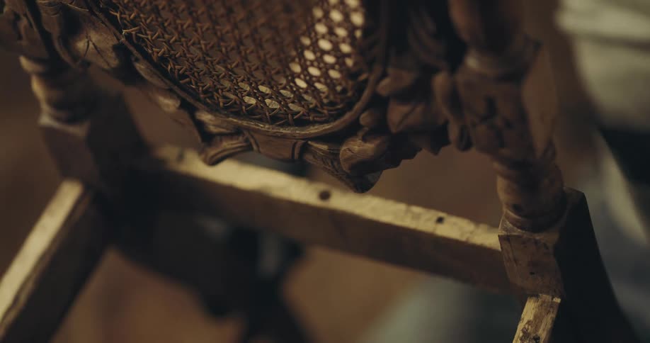 A man applies a wood stain with a rag to a carved wooden chair