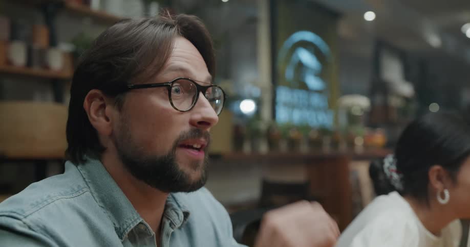 A man sitting at a table in restaurant with a group of people talks with the person sitting across from him