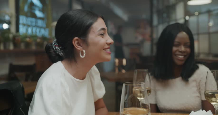 Friends sit around table in smoky bar with wine glasses laughing and talking