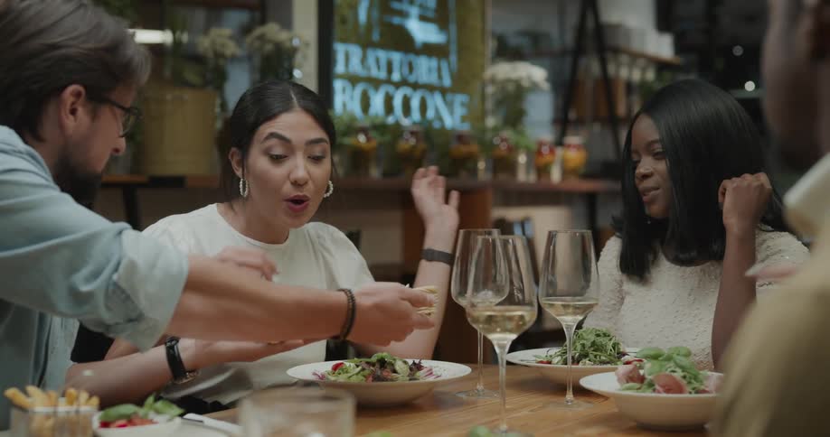 A group of people sit at a restaurant table and one man passes around the bowl of silverware