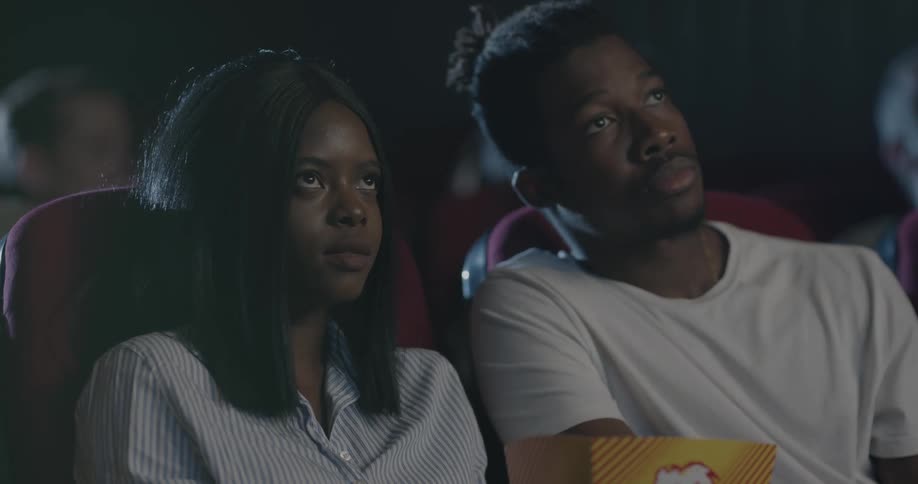 Man and woman eat popcorn and watch a movie in the movie theater