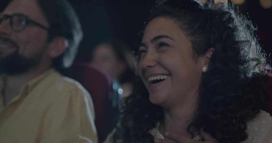 A young woman laughs while watching a movie in a cinema theater with an older man