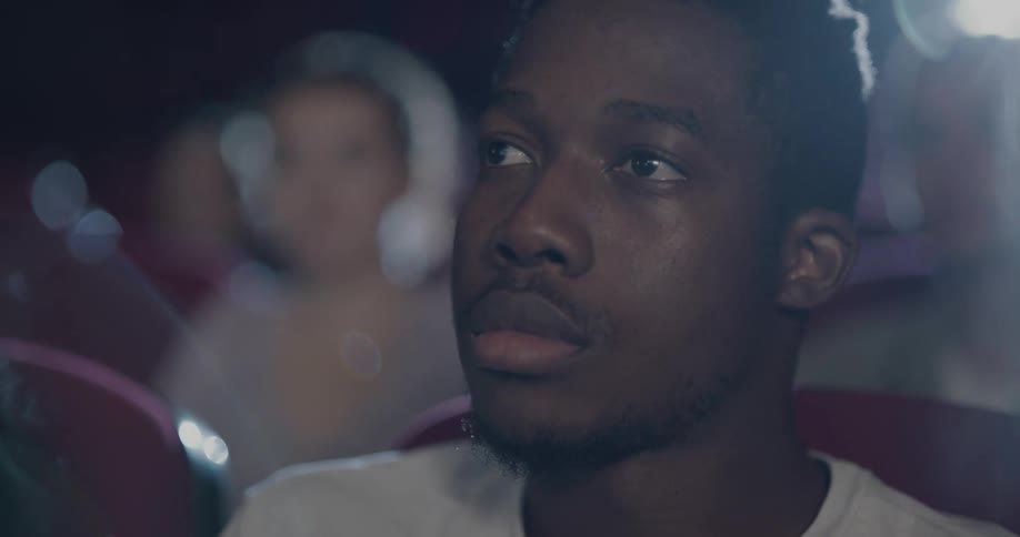 A young man watches a movie while sitting in a cinema theater