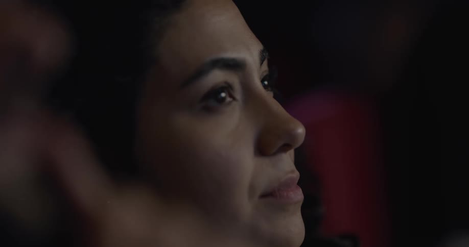 Woman with curly hair and earrings watches a movie in the movie theater
