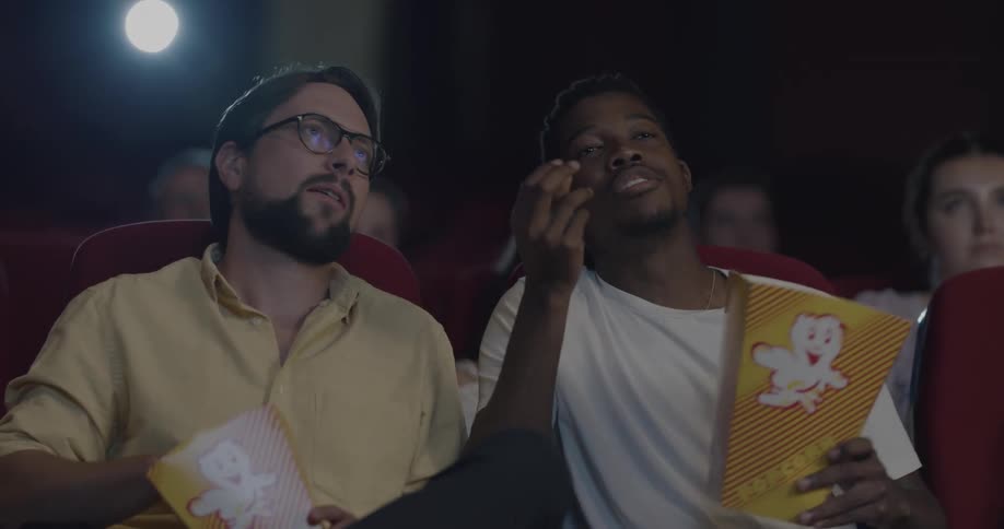 Two men talking and eating popcorn in a movie theater