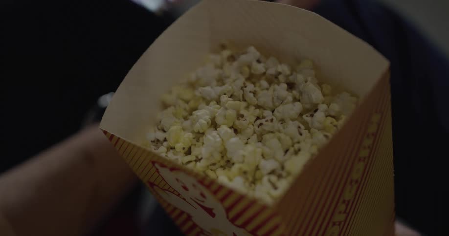 Man and womans hands take popcorn out of popcorn bag to eat in the movie theater