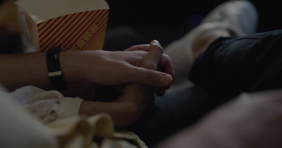 Couple sits close together holding hands with popcorn in lap