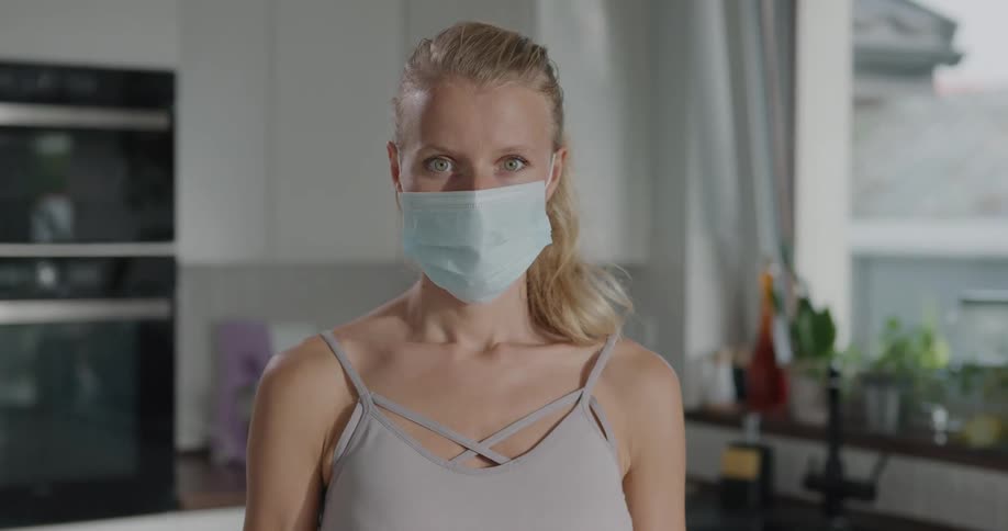 A woman standing in her kitchen with a mask on