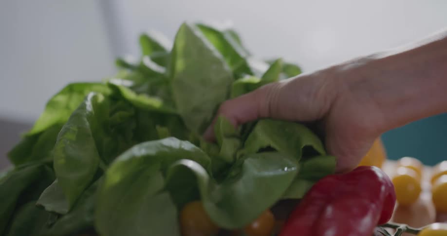 Person picks up green leafy vegetable from among other produce sitting on chopping board