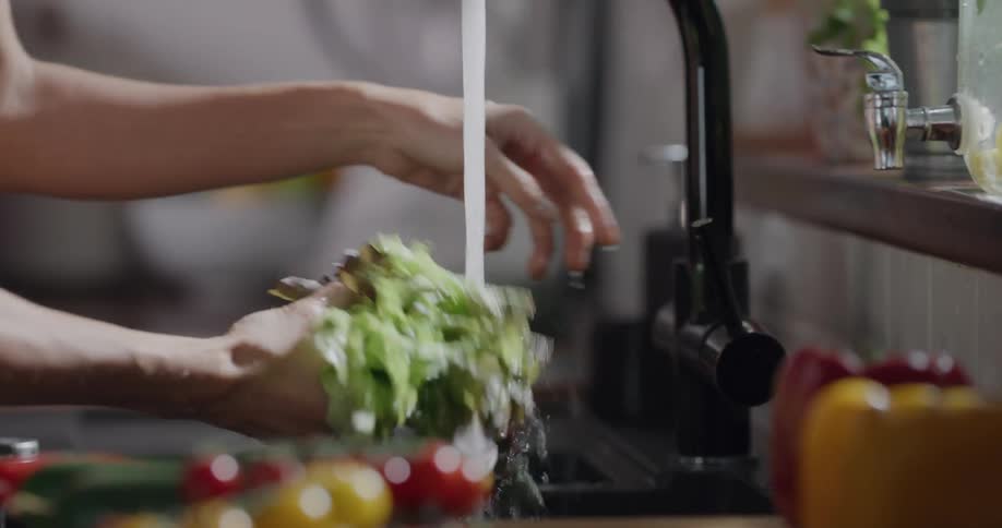 Woman wearing sport bra washes produce at kitchen sink