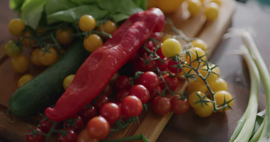 Red yellow tomatoes a cucumber and a red pepper on a cutting board in the kitchen