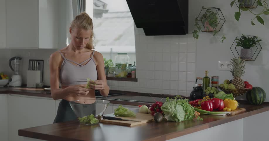 Woman standing at kitchen counter tears lettuce for salad