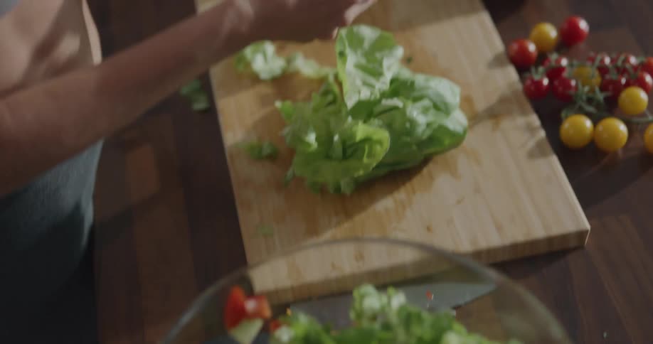 Woman tears lettuce for salad in glass bowl on wooden surface
