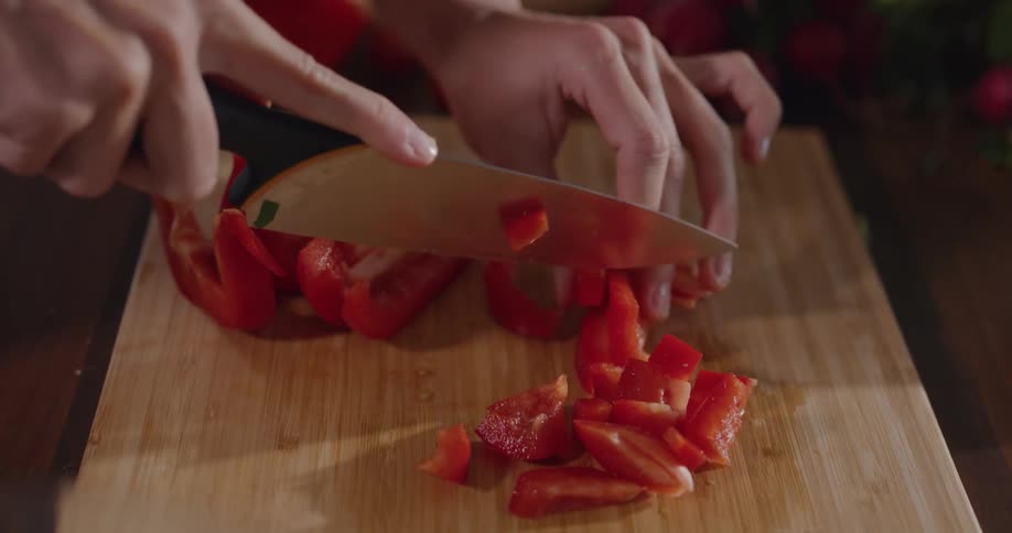 A person cutting up a red bell pepper on a wood cutting board